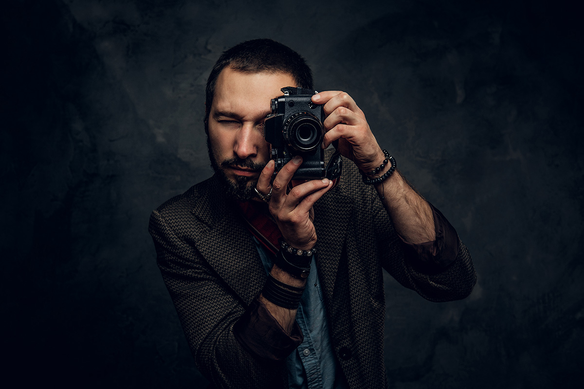 Focused young photographer is taking a photo on the dark grunge background.